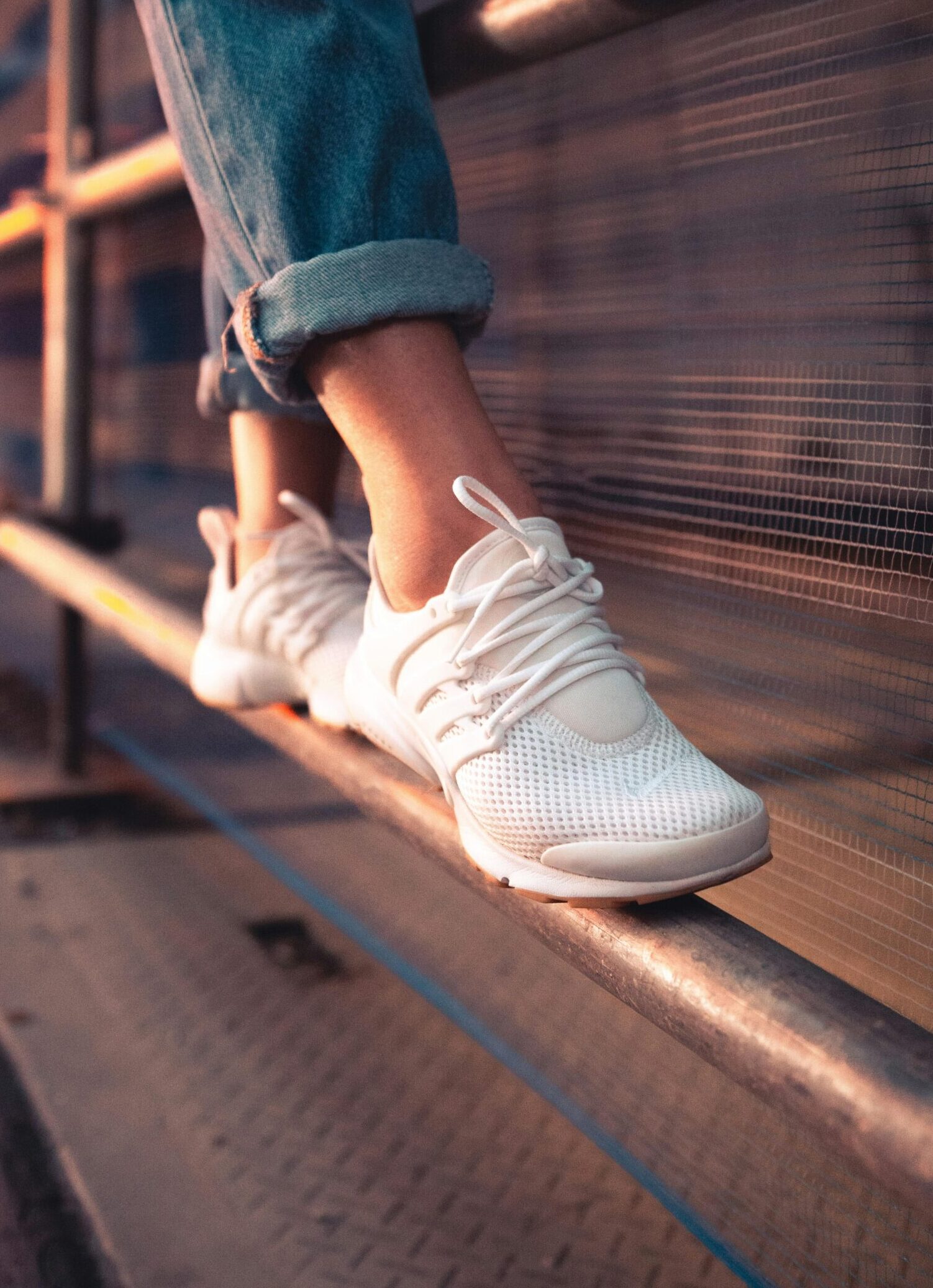 Close-up of white sneakers over a metal railing, showcasing casual style and urban fashion.